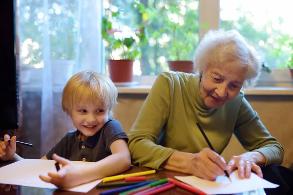 연로 한 할머니는 어린 손자가 숙제를 하도록 도와 줍니다. 할머니와 손자가 함께 그리는 모습. — 스톡 사진