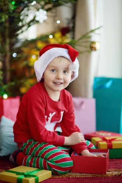 Petit garçon excité avec un cadeau de Noël sous sapin à la maison. Portrait d'enfant heureux le matin de Noël . — Photo