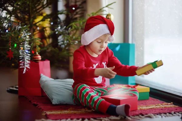 Słodki chłopczyk otwiera prezent świąteczny. Portret szczęśliwego dziecka w świąteczny poranek. — Zdjęcie stockowe