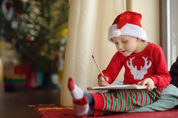 Um rapazinho a escrever a carta ao Pai Natal. Criança sonha com um presente que ele pode receber . — Fotografia de Stock