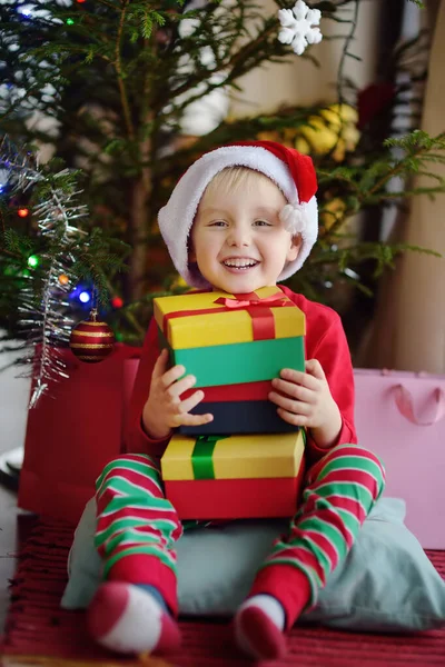 Petit garçon excité avec un cadeau de Noël sous sapin à la maison. Portrait d'enfant heureux le matin de Noël . — Photo