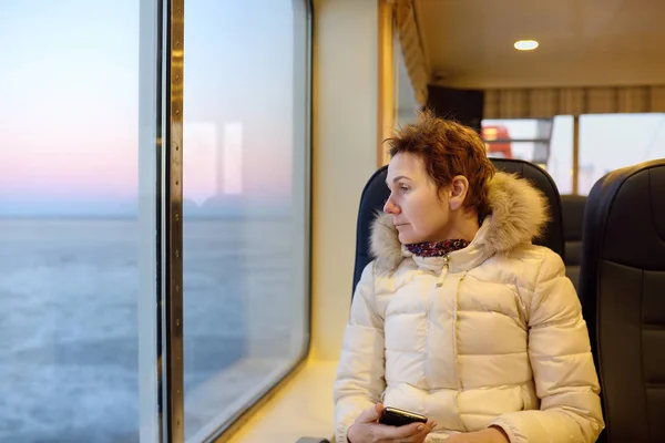 Mujer madura está mirando por la ventana a la increíble vista del mar congelado durante el cruce en el ferry . — Foto de Stock