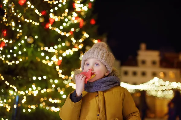 A kisfiú a nagy karácsonyfenyő mellett eszik. Karácsonyi ünnepek a híres vásár Tallinn, Észtország. — Stock Fotó