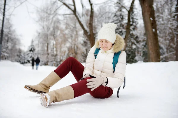 Aufnahme einer Person beim Sturz in den verschneiten Winterpark. Frau rutschte auf eisglatter Fahrbahn aus, stürzte, verletzte sich am Knie und saß im Schnee. — Stockfoto