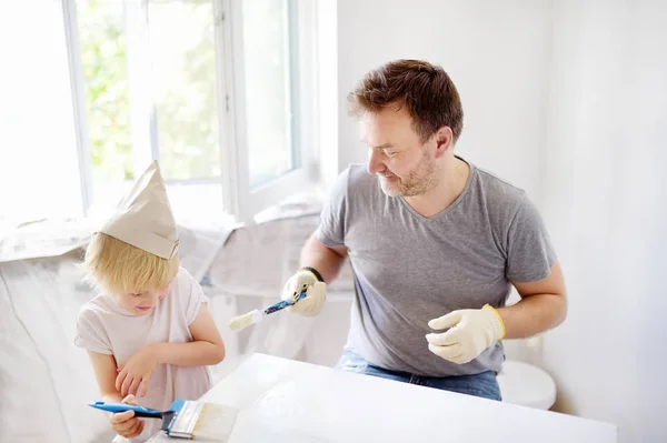 Volwassen man en kleine jongen hebben plezier met verf borstel tijdens reparatie van de kamer samen. — Stockfoto