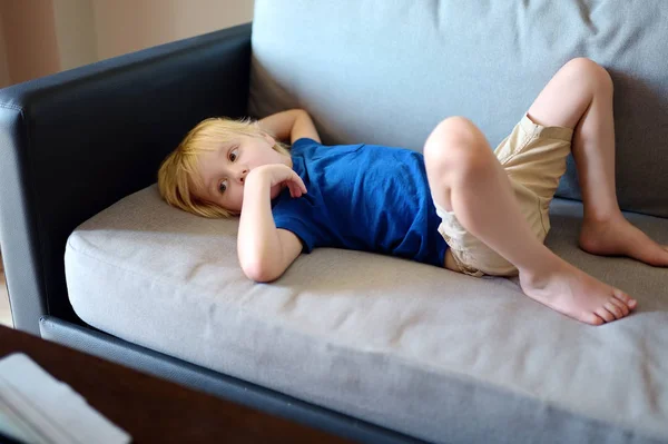 Malý chlapec ležel na gauči a sledoval kreslené seriály podle tabletu. Děti a pomůcky. Závislost. — Stock fotografie
