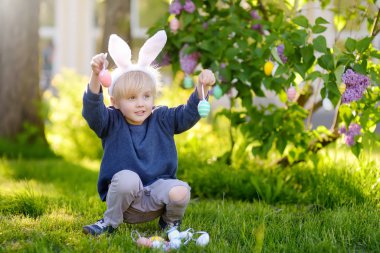 Paskalya günü bahar parkında tavşan kulağı takan güzel bir çocuk paskalya yumurtası arıyor..