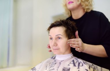 Kuaför, güzellik salonunda orta yaşlı bir kadın için saç stili yapıyor. Kadınlar için kısa kestirme.