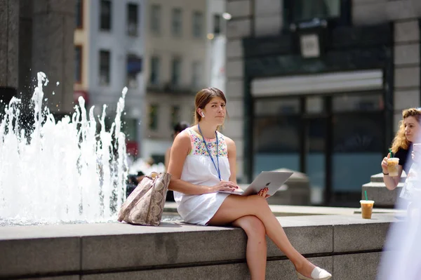 New York, Usa - 10 juli 2019: Charmig kvinna sitter med sin laptop nära fontänen under lunchrasten — Stockfoto