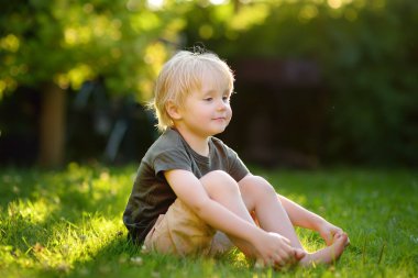 Güzel çocuk çimlere bir güneşli yaz gününde oturuyor. Mutlu çocukluk. Doğa çocuklarda.
