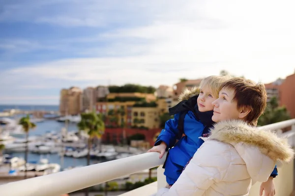 Grandmother and her little grandchild looking on yachts and boats in port of Monaco in winter day. Travel for family with kids during school holidays.
