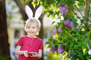 Pretty little boy wearing bunny ears hunting for eggs in spring park on Easter day.Traditional easter festival outdoors. clipart