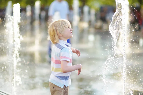 晴れた夏の日に噴水のウォータージェットの間の広場で小さな男の子が遊んでいます 市内の子供のためのアクティブな夏のレジャー — ストック写真