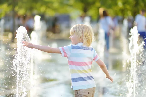 晴れた夏の日に噴水のウォータージェットの間の広場で小さな男の子が遊んでいます 市内の子供のためのアクティブな夏のレジャー — ストック写真