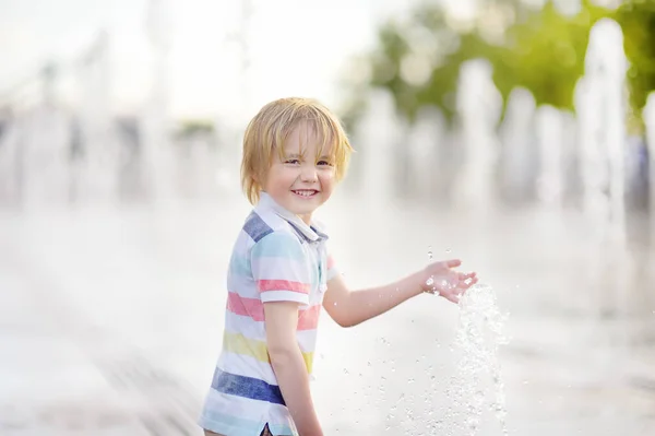 晴れた夏の日に噴水のウォータージェットの間の広場で小さな男の子が遊んでいます 市内の子供のためのアクティブな夏のレジャー — ストック写真