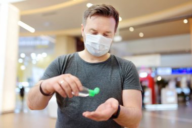 Tek kullanımlık tıbbi maske takan adam havaalanında, süpermarkette ya da başka bir yerde dezenfekte edici ile ellerini dezenfekte ediyor. Koronavirüs salgını sırasında güvenlik. Virüs salgını..