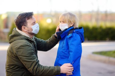 Koruyucu maske takan olgun bir adam oğlunun yüzüne maske takar. Havaalanında, süpermarkette ya da başka bir yerde. COVID-19 salgını sırasında güvenlik. Virüs salgını..