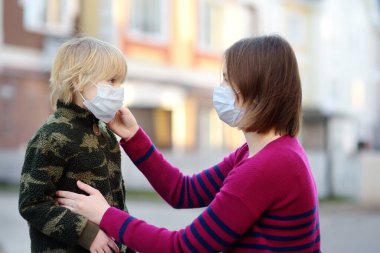 Koruyucu maske takan genç bir kadın havaalanında, süpermarkette ya da başka bir yerde oğluna maske takıyor. COVID-19 salgını sırasında güvenlik. Virüs salgını var. Koronavirüs salgını.