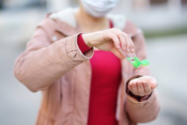Woman wearing disposable medical face mask makes disinfection of hands with sanitizer in airport, supermarket or other public place. Safety during COVID-19 outbreak. Epidemic of virus covid. Pandemic. clipart