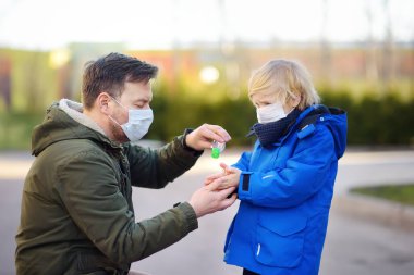 Koruyucu maske takan yetişkin bir adam ve küçük bir çocuk havaalanında, süpermarkette ya da başka bir yerde dezenfektanla elleri dezenfekte eder. COVID-19 salgını sırasında güvenlik. Virüs salgını.