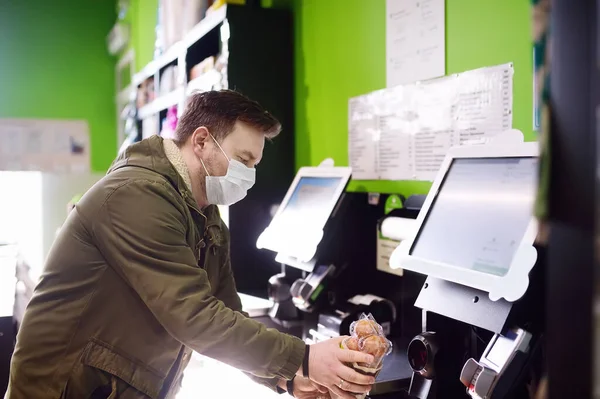 Mature man is scanning grocery items with bar code scanner in supermarket contactless method by checkout counter. Safety during COVID-19 outbreak in public places. Epidemic of virus covid. Coronavirus