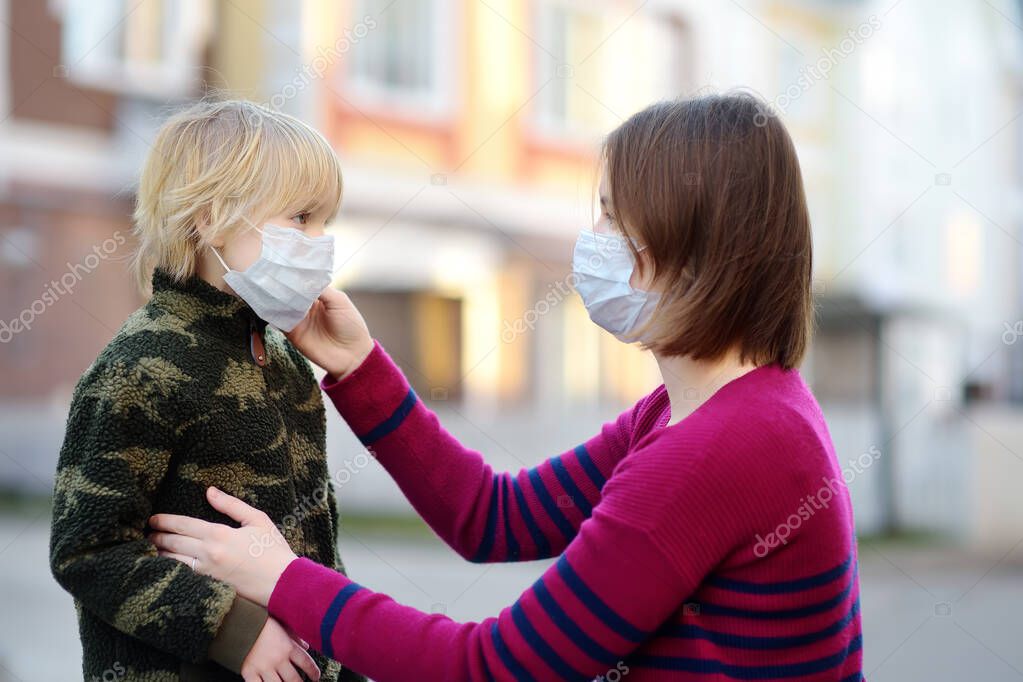 Young woman wearing a protective mask puts a face mask on a his son in airport, supermarket or other public place. Safety during COVID-19 outbreak. Epidemic of virus covid. Coronavirus pandemic.