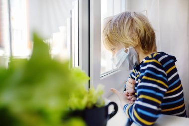 Küçük çocuk koronavirüs salgını sırasında pencereye bakıyordu. İletişim ve yürüme olmadan sıkıcı bir çocuk. Karantinaya alınana kadar evde kal. Sosyal mesafeyi korumak.
