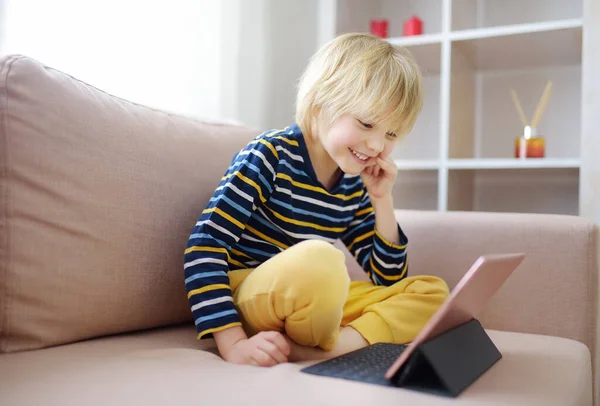 Preschooler boy is watching movies or cartoon movie from tablet sitting on couch. Entertainments for little kids while coronavirus pandemic. Stay at home during quarantine.