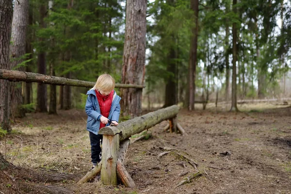 小さな男の子が春に森の中を歩いていると 大きな伐採された丸太に小さなペンナイフで枝を見た 子供のための野外活動 — ストック写真