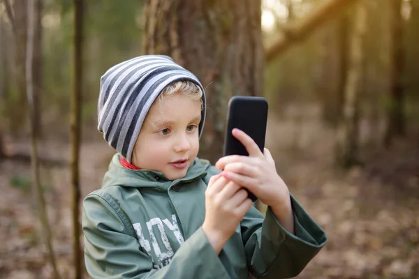 春や秋に森の中を歩くときにスマートフォンで写真やビデオ通話を行う小さな男の子 近代技術 — ストック写真