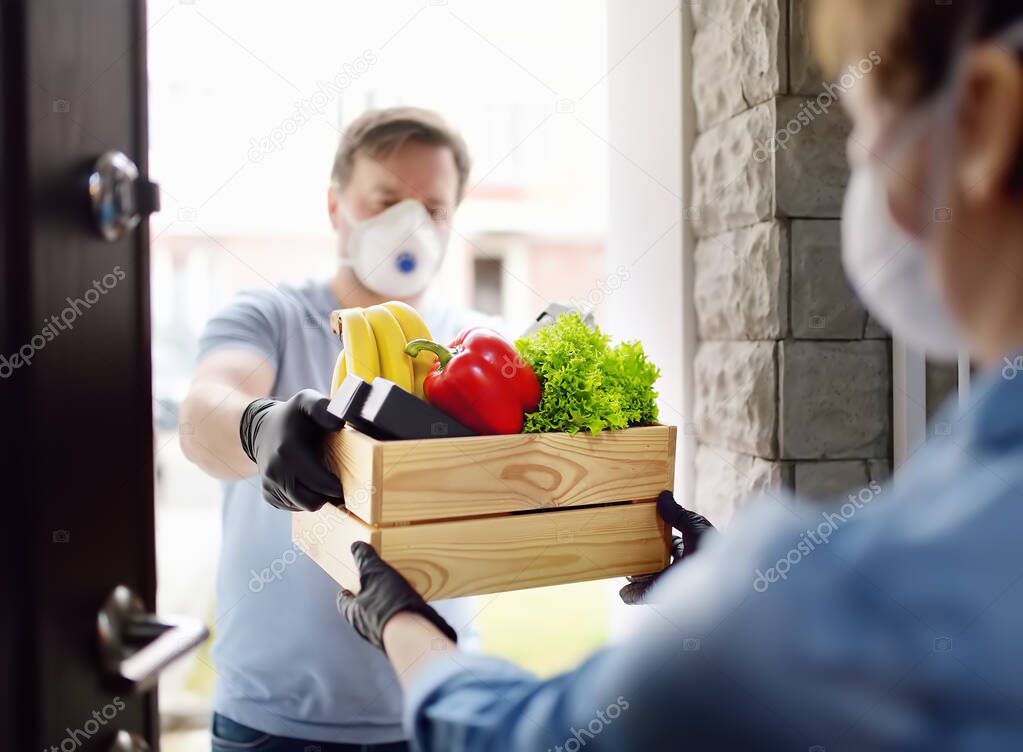 Courier or volunteer delivering shopping to woman during coronavirus quarantine. Woman customer receiving online order from courier at home. Food delivery service on door. Express food delivery.