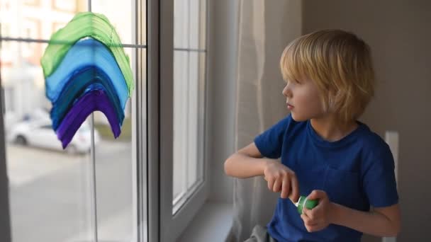 コロナウイルスの隔離中に窓の虹を描く小さな男の子 レインボーサインは希望の象徴ですすべてがうまくいくことを意味しますコロナウイルスをロックダウンするために家にいてください — ストック動画