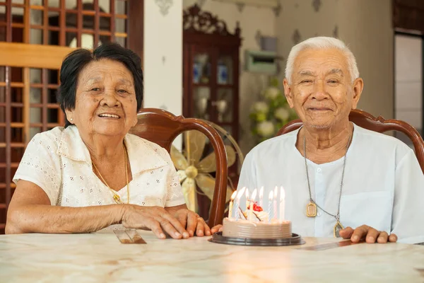 Aziatische senior paar houden een taart en lachend in woonkamer — Stockfoto