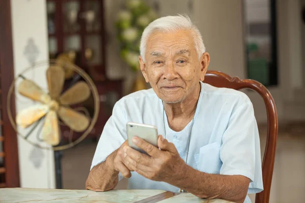 Lycklig asiatiska senior man använder mobiltelefonen hemma — Stockfoto