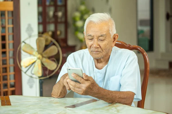 Ευτυχισμένος Ασίας ανώτερος άνθρωπος που χρησιμοποιούν το κινητό τηλέφωνο στο σπίτι — Φωτογραφία Αρχείου