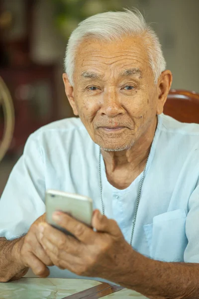 Lycklig asiatiska senior man använder mobiltelefonen hemma — Stockfoto