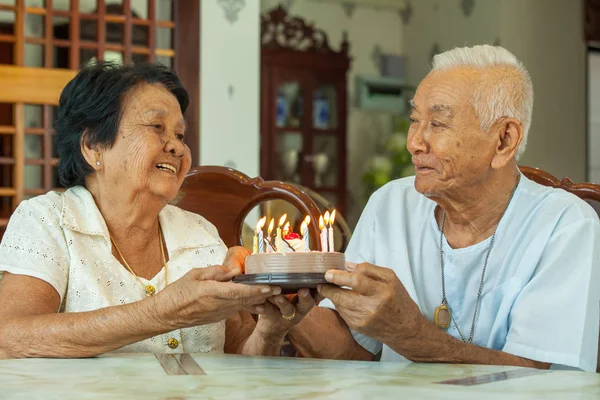 Asiático casal sênior segurando um bolo e sorrindo na sala de estar — Fotografia de Stock