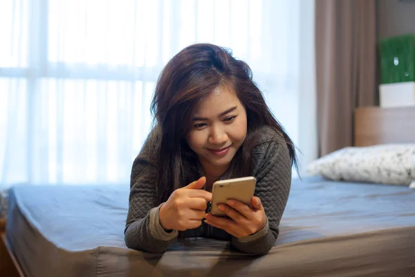 Szczęśliwa młoda kobieta azjatyckich leżącego przy użyciu smartfona — Zdjęcie stockowe