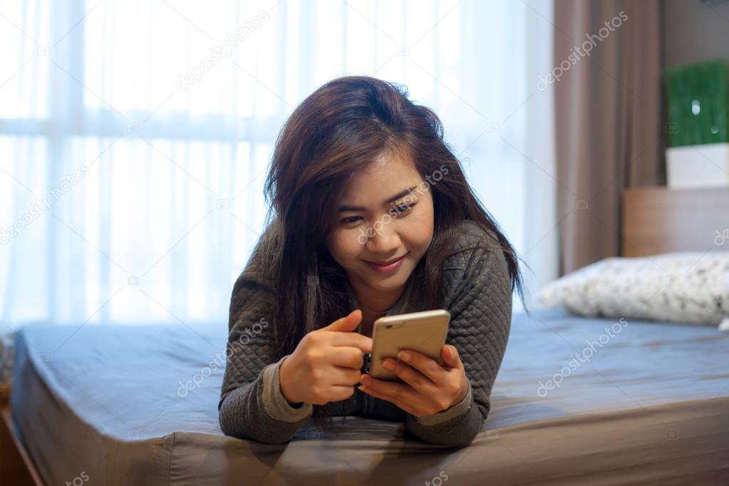 Happy asian young woman lying using smart phone