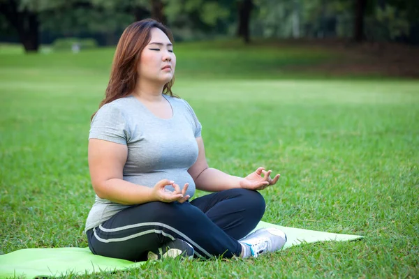 Plus size woman practicing yoga on green grass — Stock Photo, Image