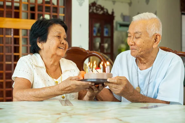 Casal de idosos segurando um bolo e sorrindo na sala de estar — Fotografia de Stock