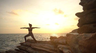 Gün batımında deniz kıyısında egzersiz yapan yoga yapan Asyalı kadın silueti.