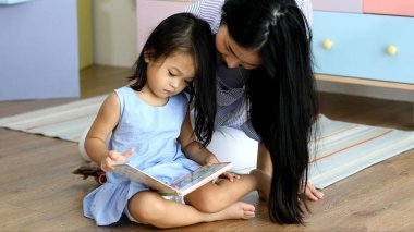 Mutlu Asyalı aile anne ve kızı birlikte kitap okuyorlar.