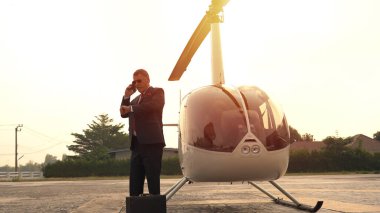 İş adamı özel helikopterin yanında cep telefonuyla konuşuyor.