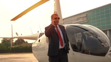 İş adamı özel helikopterin yanında cep telefonuyla konuşuyor.