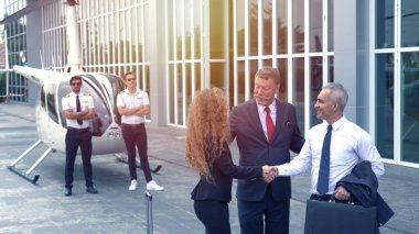 İş adamı ve pilot iniş noktasında küçük özel bir helikopterin yanında konuşuyorlar.