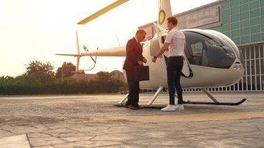 İş adamı ve pilot iniş noktasında küçük özel bir helikopterin yanında konuşuyorlar.