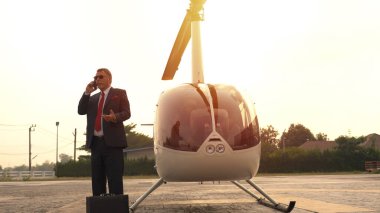 İş adamı özel helikopterin yanında cep telefonuyla konuşuyor.