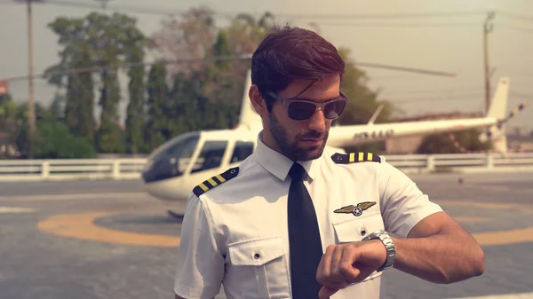 Portrait of commercial pilot in uniform standing near small private helicopter