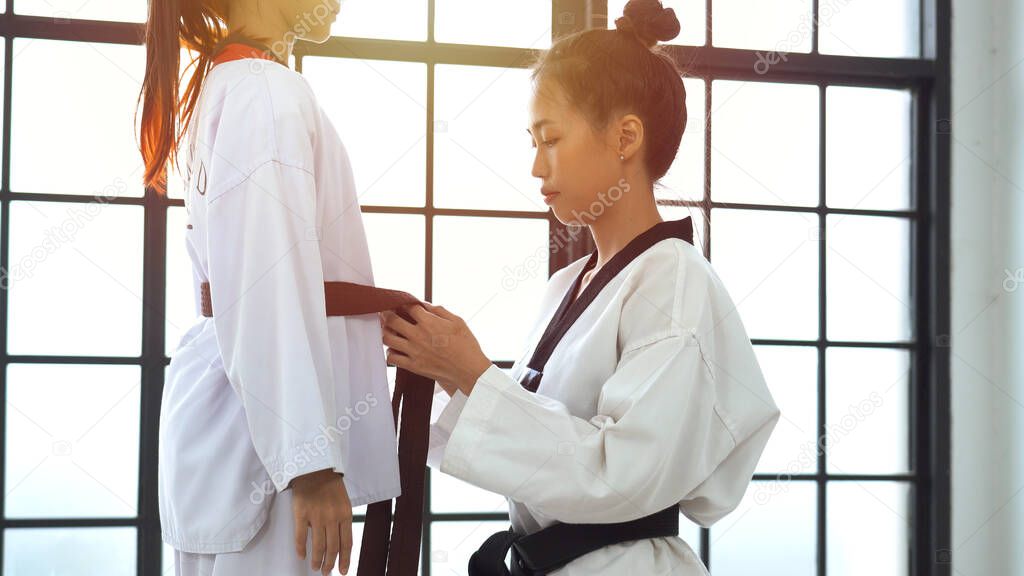 Trainer helping asian girl to adjust training costume for taekwondo